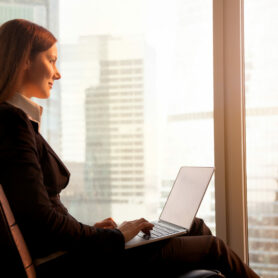 Side view of attractive businesswoman enjoying sunset, sitting comfortably in office chair with laptop on her knees, feeling inspired, calm and motivated for great achievements in career and life